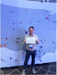 Cody Ingle poses with a sign that reads, “I am working on Violence in Sioux Falls, SD and I see hope for America’s health in LGBTQ+ Health and suicide prevention.”